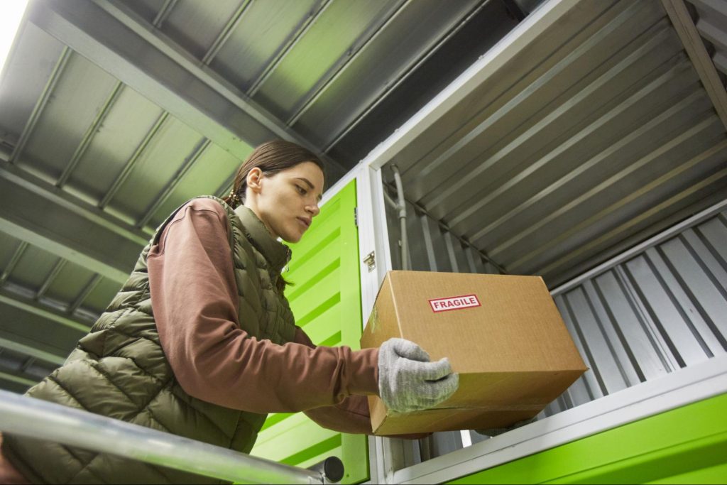 A woman wearing protective gloves is loading a box into a shipping container to be sent out