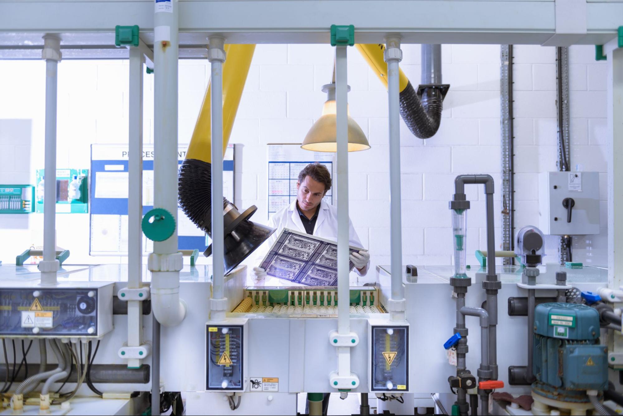 Man looking at a PCB board in a factory with machinery
