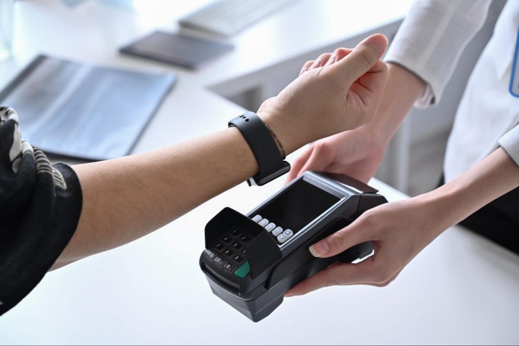Man holds his smart watch over a card scanner to pay