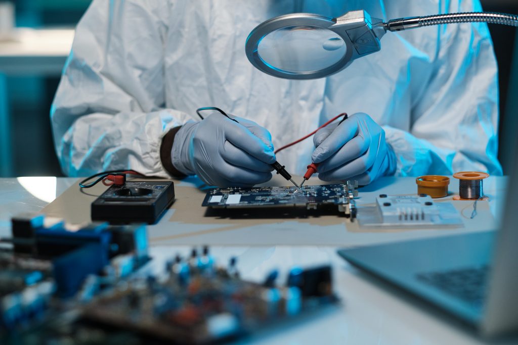 Gloved technician soldering details of a motherboard with tweezers