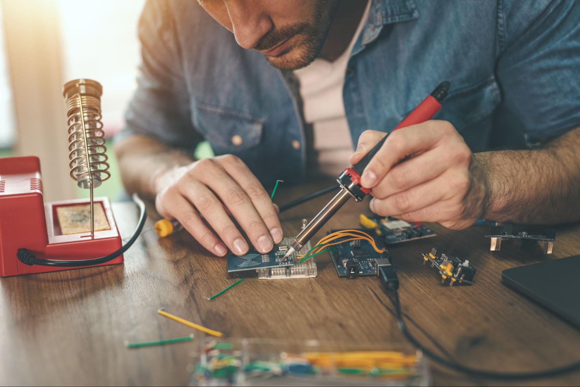 Engineer or technician is focused on repairing electronic circuit board with soldering iron.