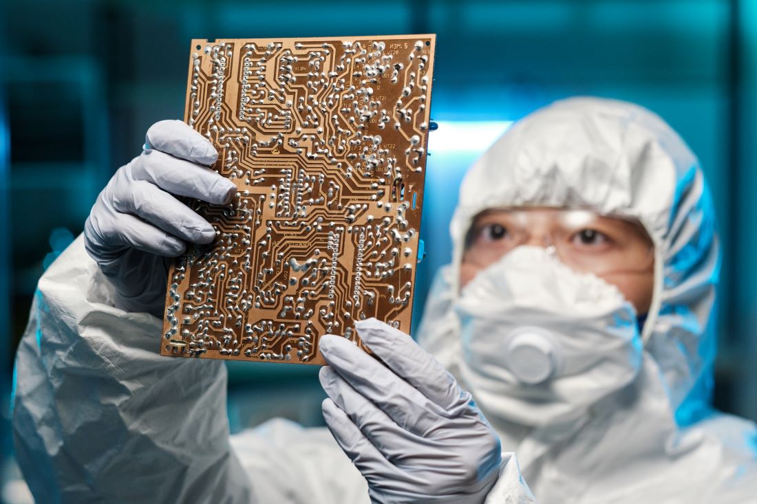 Gloved female specialist in protective coveralls holding circuit board