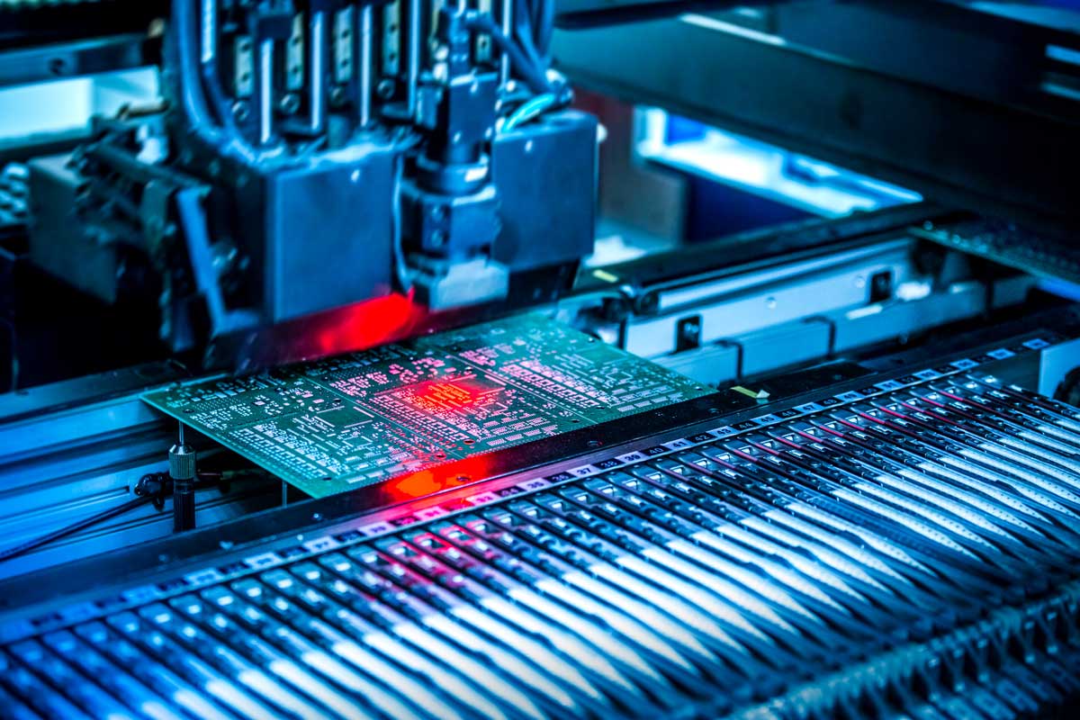 Automated SMT machine placing components on a printed circuit board with red laser alignment