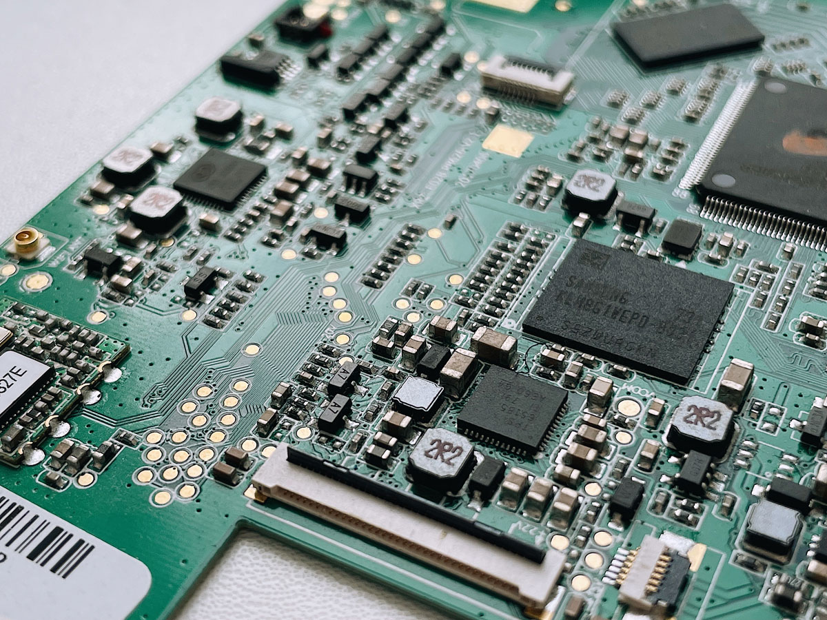 Close-up view of a green printed circuit board with various microchips, capacitors, and electronic components