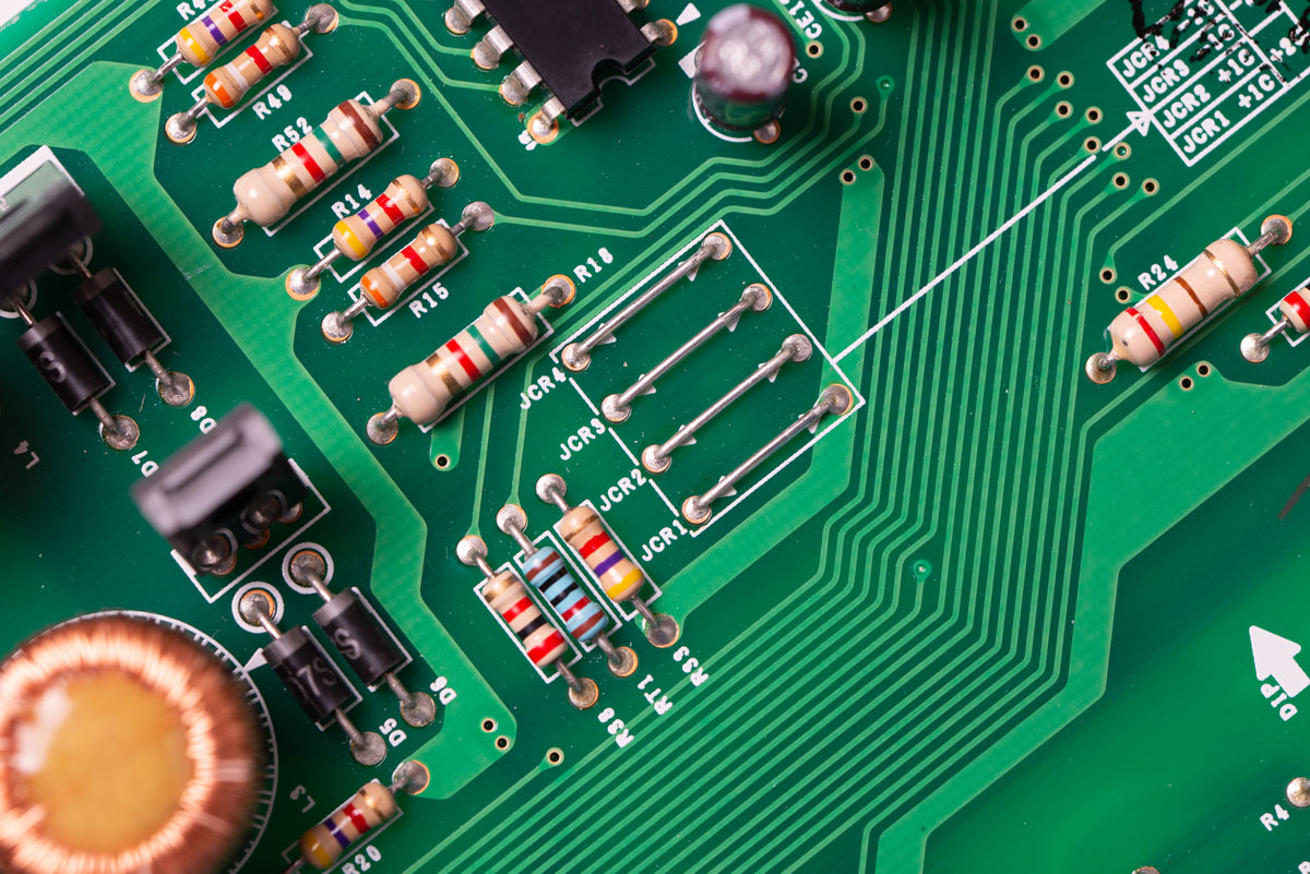Close-up of a green circuit board showing resistors, capacitors, and intricate electronic pathways